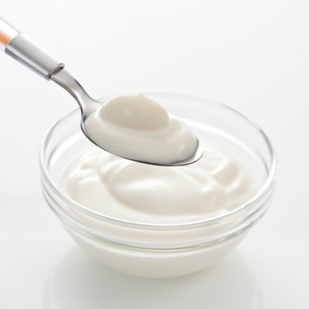 Bowl and spoon with yogurt on white background, close up